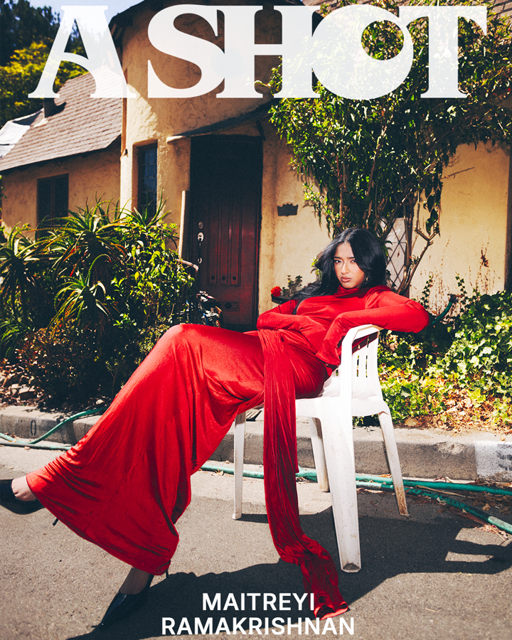 Maitreyi Ramakrishnan in a red dress posed in a plastic chair in the sunlight with text that says 'A Shot' along the top of the image